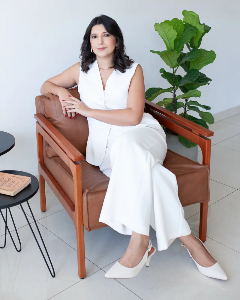 Andressa Cristina de conjunto branco, sentada numa poltrona